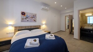 A modern hotel room with a large bed, a painting on the wall, and a bathroom visible through an open door. - Ilianas Home - Kalamata Mediterraean Suites & Villas (Kalamata)