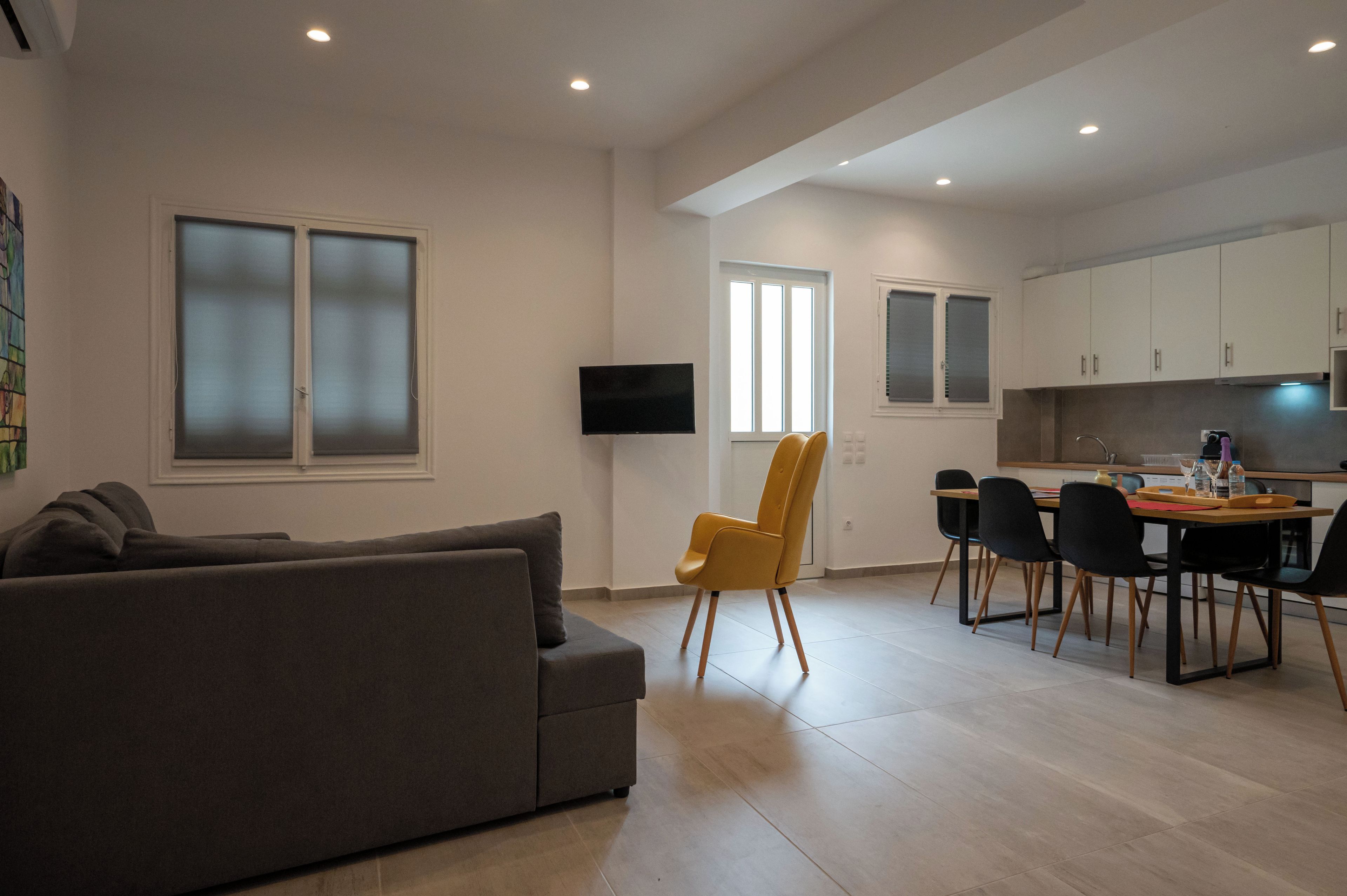 A modern living room with a grey sofa, a yellow chair, and a dining area with a table and chairs.