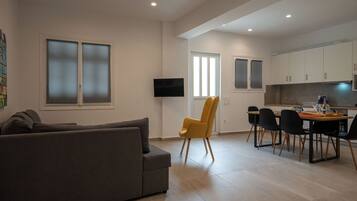 A modern living room with a grey sofa, a yellow chair, and a dining area with a table and chairs.