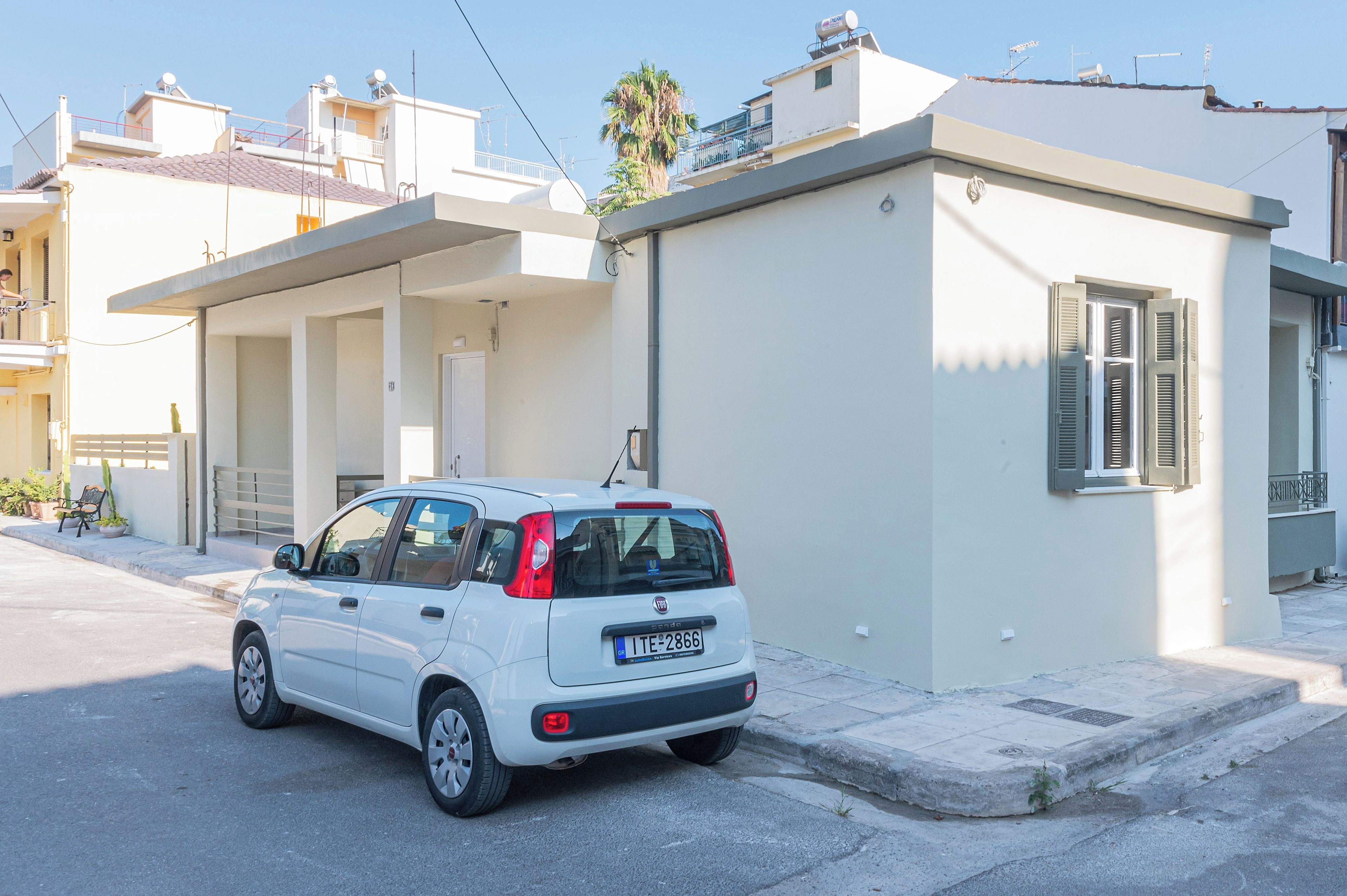 A white compact car parked in front of a building with a balcony and a door.