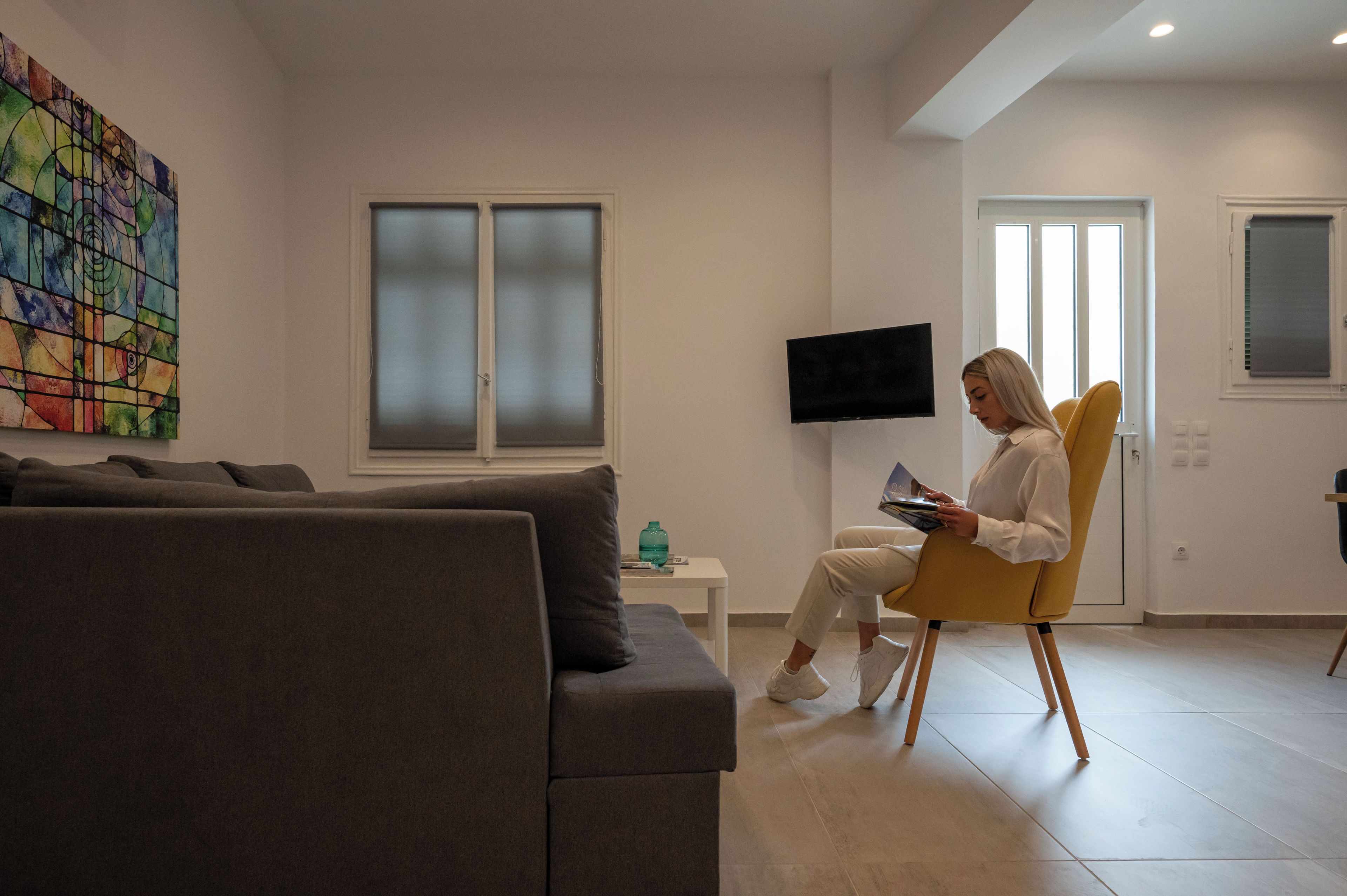 A modern living room with a grey sofa, a yellow chair, a flat-screen TV, and a colorful abstract painting on the wall.