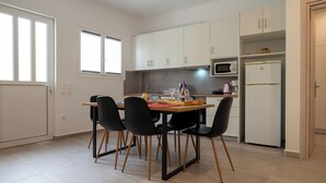 Una cocina compacta con armarios blancos, microondas, refrigerador y un comedor con mesa y sillas.