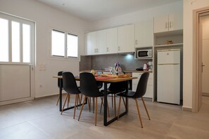 Een kleine keuken met witte kastjes, een magnetron, een koelkast, en een eethoek met een tafel en stoelen.