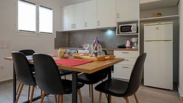 A modern kitchen with white cabinets, a microwave, a refrigerator, and a dining area with a table and chairs.