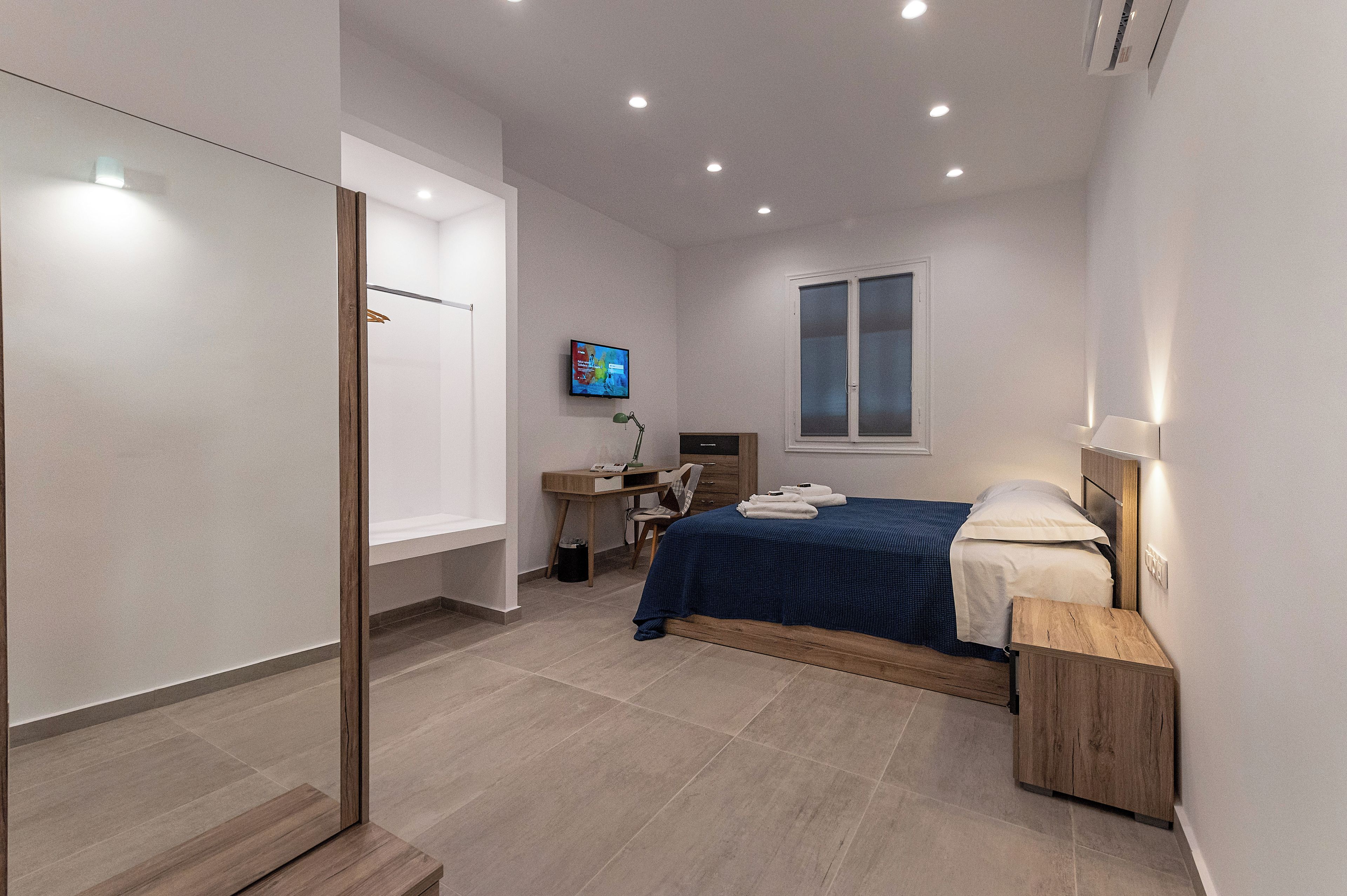 Ein modernes Schlafzimmer mit Bett, Nachttisch, Schreibtisch, Stuhl und einem Fernseher an der Wand.