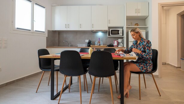 A modern kitchen with white cabinets, a microwave, and a dining area with a table and chairs. - Ilianas Home - Kalamata Mediterraean Suites & Villas (Kalamata)
