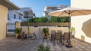 Un espacio al aire libre con mesa, sillas, una bicicleta y plantas en macetas.
