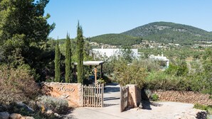 A gated entrance with a stone wall and a wooden gate, leading to a building with a white facade and a mountain in the background. - Es Cucons Rural Hotel (Sant Antoni de Portmany)