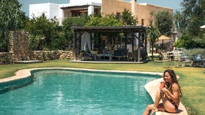 A swimming pool with a person sitting on the edge. There is a building with a covered patio in the background. - Es Cucons Rural Hotel (Sant Antoni de Portmany)