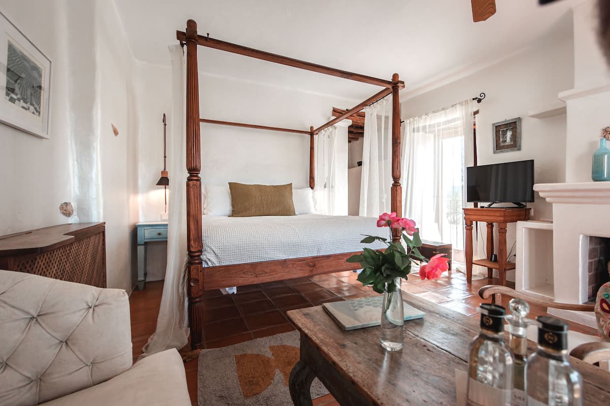 A four-poster bed with a wooden frame, a bedside table with a lamp, and a vase with flowers.