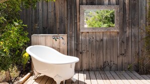 A wooden deck with a white freestanding bathtub and a window with a view of greenery. - Es Cucons Rural Hotel (Sant Antoni de Portmany)