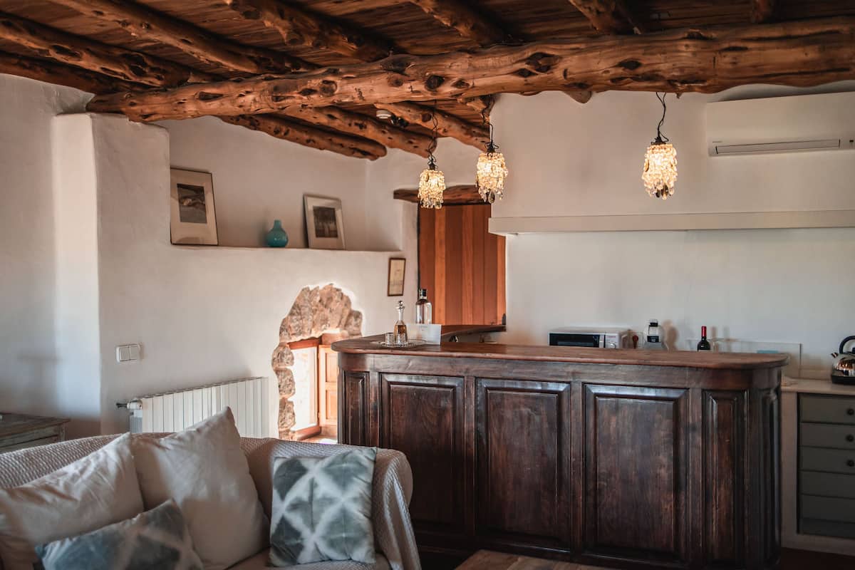 A rustic kitchen with wooden beams, a bar area, and a cozy seating area with cushions.