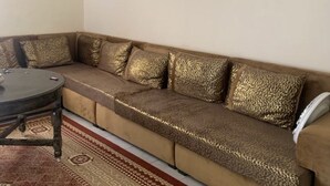 Olohuoneessa on beige sohva, kuviollisia koristetyynyjä, pyöreä sohvapöytä ja kuviollinen matto.