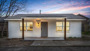 A single-story house with a front porch, a door, and two windows with shutters. - Downtown Access | Spacious | Family Space (Starkville)