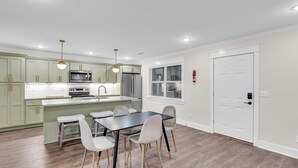 A modern kitchen with a dining area, featuring a central island, stainless steel appliances, and a white door. - Downtown Access | Spacious | Family Space (Starkville)
