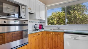 Una cocina con electrodomésticos de acero inoxidable, armarios de madera, un ventanal con vista a árboles y una cafetera.