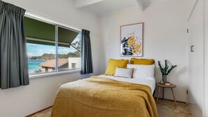 A bedroom with a bed, a window with curtains, a framed picture, and a small table with a plant. - Beach House On Booth ~ The Quintessential Beach House for the Family Get-away (Narrawallee)