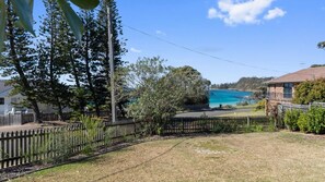 A residential area with a view of a blue water body, surrounded by trees and a wooden fence. - Beach House On Booth ~ The Quintessential Beach House for the Family Get-away (Narrawallee)