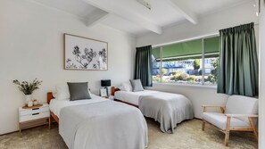 A hotel room with two beds, a desk, a chair, a window with curtains, and a framed picture on the wall. - Beach House On Booth ~ The Quintessential Beach House for the Family Get-away (Narrawallee)