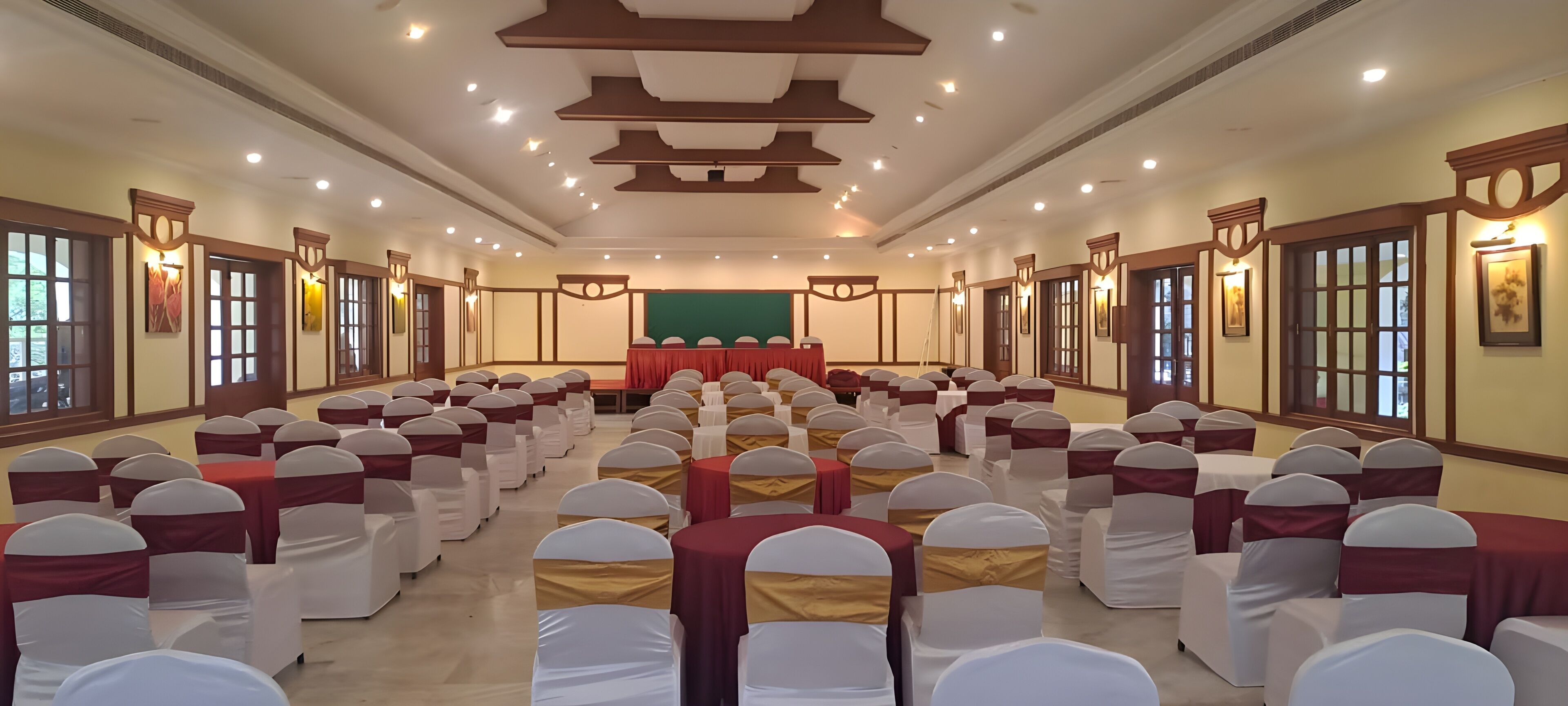 A conference room with rows of chairs, a stage, and wall-mounted lighting.