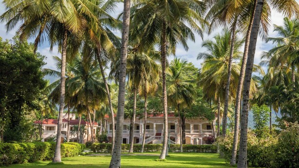 A hotel with a central courtyard surrounded by palm trees, a red-roofed building, and a well-maintained lawn. - Avana Resort (Mettupalayam)