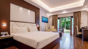 A hotel room with a large bed, a desk, a chair, and a view of the outdoors. - Avana Resort (Mettupalayam)