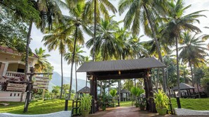 A resort entrance with a covered walkway, palm trees, and directional signs for amenities like a garden restaurant and health club. - Avana Resort (Mettupalayam)