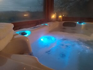 A hot tub with blue lighting, wooden walls, and a view of the outdoors. - Domaine du Mas Naut (Conques-en-Rouergue)
