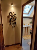 Un pasillo con un adorno en la pared, un tragaluz y un baño visible a través de una puerta abierta.