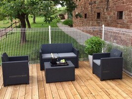 Un patio al aire libre con un sofá de mimbre oscuro, dos sillones y una mesa de centro. Hay una botella de champán sobre la mesa.