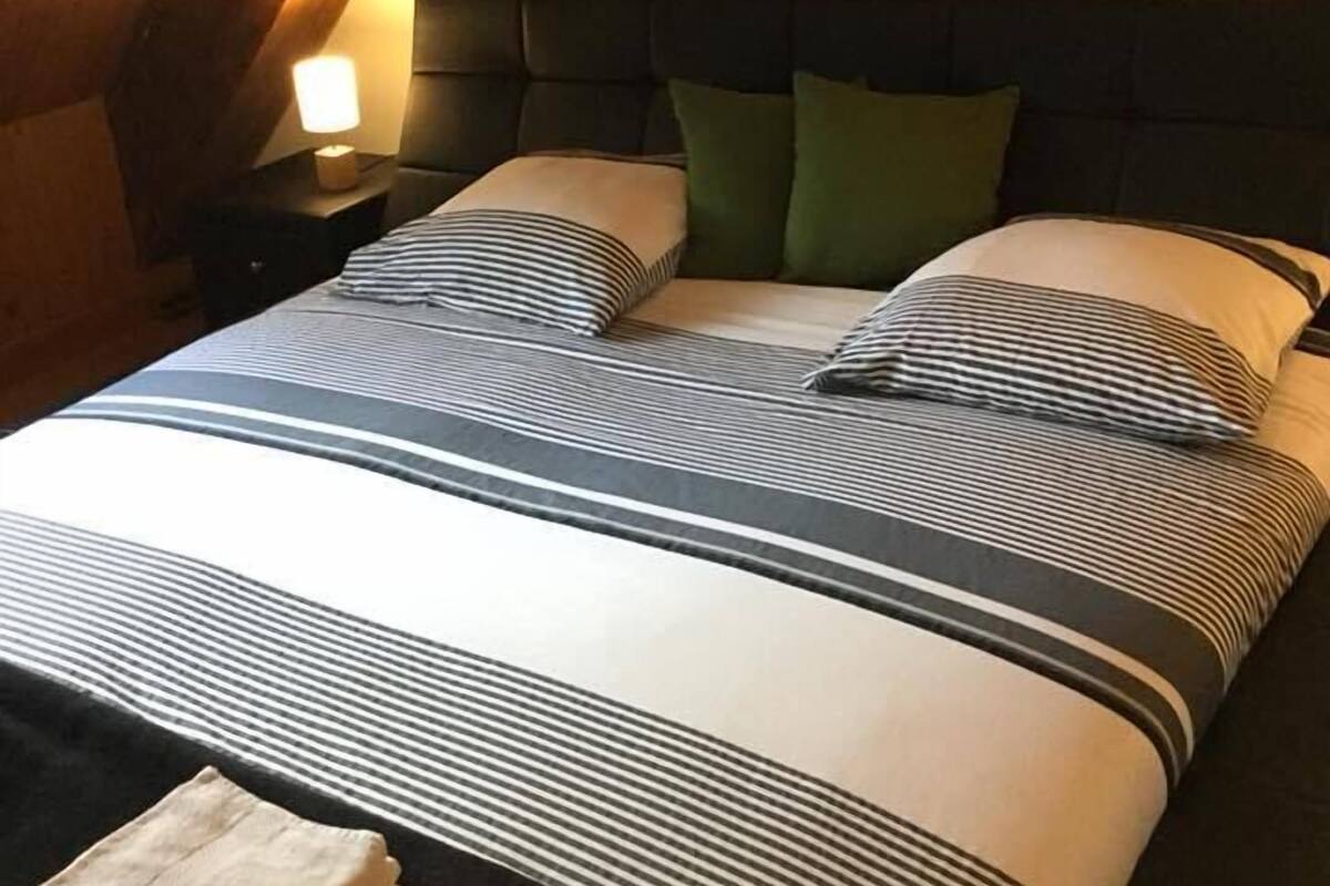 Une chambre à coucher avec un lit, des oreillers, une table de chevet, une lampe et une étagère fixée au mur.