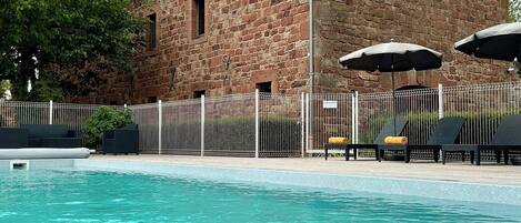 A stone building with a swimming pool, outdoor seating, and a fenced area.