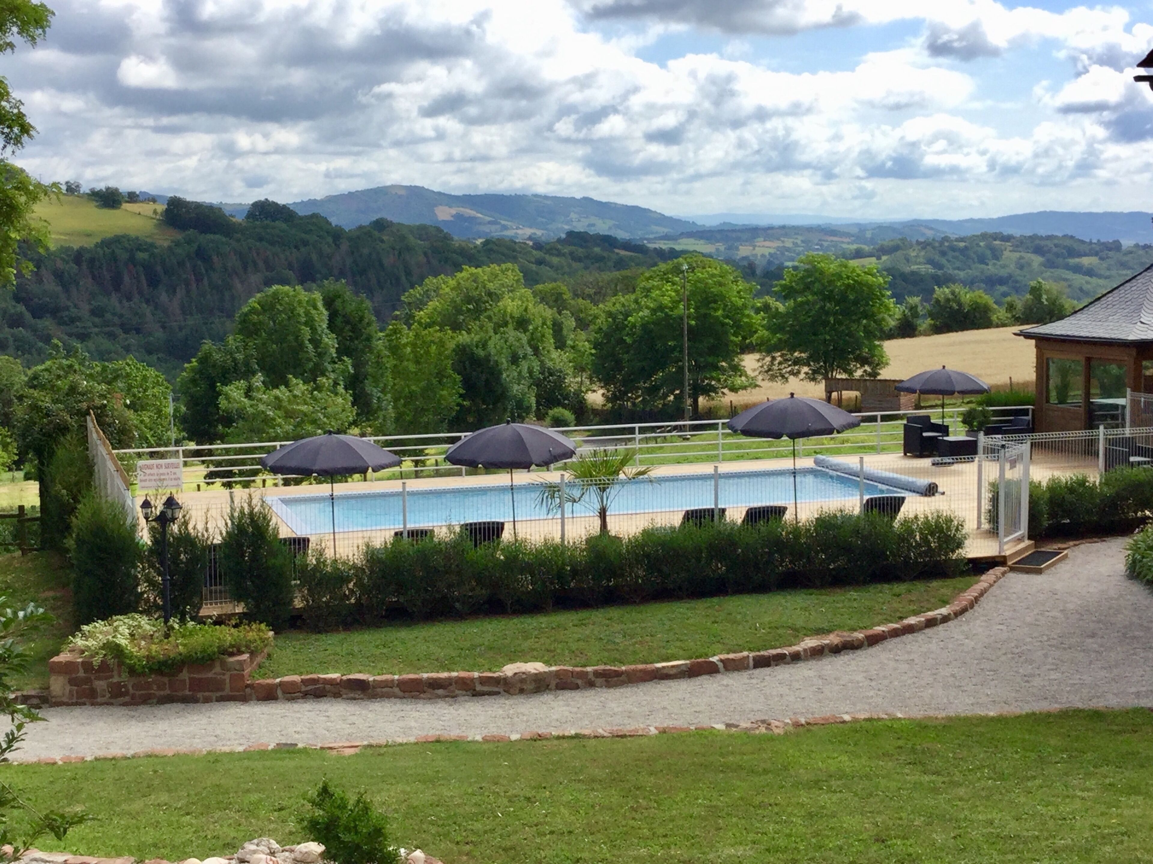 A swimming pool with umbrellas, surrounded by a fenced area with a view of distant hills.