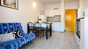 Een knus leefruimte met een bank, eettafel, stoelen, een kitchenette en een kleine koelkast.