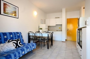 A compact living space with a sofa, dining table, chairs, a kitchenette, and a small refrigerator.