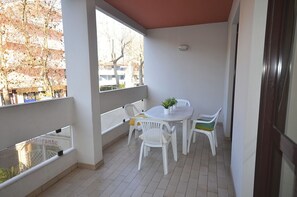 A balcony with a table and chairs, a potted plant, and a view of trees and buildings.