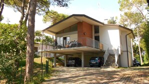 A two-story house with a balcony, a covered carport, and a staircase leading to the upper floor. - Charming villa with a hot tube (Lignano Sabbiadoro)