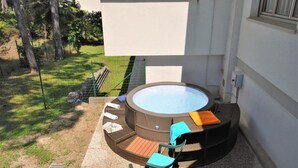 A hot tub with seating and a small table, surrounded by a grassy area and a building. - Charming villa with a hot tube (Lignano Sabbiadoro)