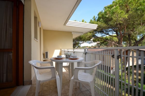 A balcony with a table and chairs, a railing, and a view of trees.
