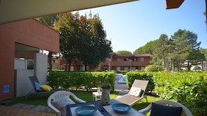 Un espace extérieur aménagé en terrasse, avec une table pour deux, entouré de fauteuils confortables et d’un petit jardin.