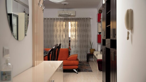 A modern living room with a sofa, a dining table, and a kitchen area with cabinets and a refrigerator.