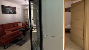 A compact living space with a modern white refrigerator, a red sofa, and a glass cabinet.