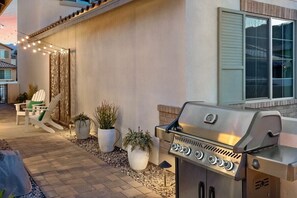 A patio with a grill, outdoor seating, and decorative lights. - Desert Escape | Private Fire Pit & Pool Bliss (La Quinta)