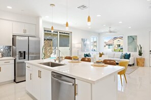 A modern kitchen with a central island, stainless steel appliances, and a dining area with a sofa and chairs. - Desert Escape | Private Fire Pit & Pool Bliss (La Quinta)
