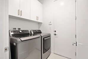 A laundry room with two washing machines and a dryer, white cabinets, and a white door. - Desert Escape | Private Fire Pit & Pool Bliss (La Quinta)