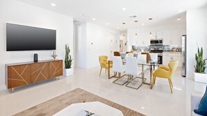 A modern living room with a flat-screen TV, a wooden cabinet, and a dining area with yellow chairs. - Desert Escape | Private Fire Pit & Pool Bliss (La Quinta)