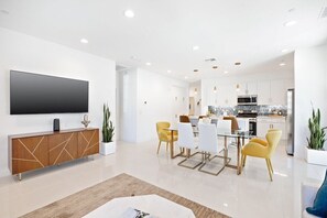 A modern living room with a flat-screen TV, a wooden cabinet, and a dining area with yellow chairs. - Desert Escape | Private Fire Pit & Pool Bliss (La Quinta)