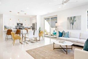 A modern kitchen with white cabinets, a dining area with a glass table, and a living room with a white sofa and a coffee table. - Desert Escape | Private Fire Pit & Pool Bliss (La Quinta)