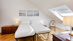A bedroom with a loft-style ceiling, two beds, wooden nightstands, a chair, and a desk with a lamp. - Seaview Apartment With Garden by Wonderful Italy (Recco)