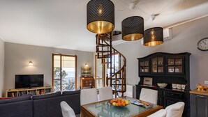 A modern living room with a spiral staircase, a dining table with chairs, a television, and a large cabinet. - Seaview Apartment With Garden by Wonderful Italy (Recco)